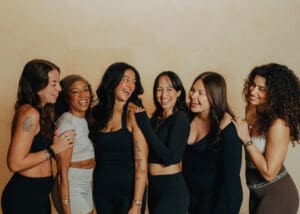 Group of six women in neutral athletic wear smiling together during Pilates branding photoshoot in Orlando studio.