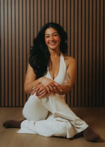 Portrait of Pilates instructor in a white set sitting on the studio floor against a wood slat wall, photographed for personal branding and fitness photography.