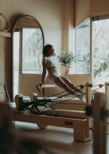 Pilates instructor performing a reformer exercise near large windows at Solace Studio in Orlando, photographed with soft natural light for wellness brand photography.
