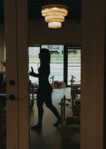 Silhouette of Pilates instructor walking through reformer studio under chandelier lighting at Solace Studio in Orlando.