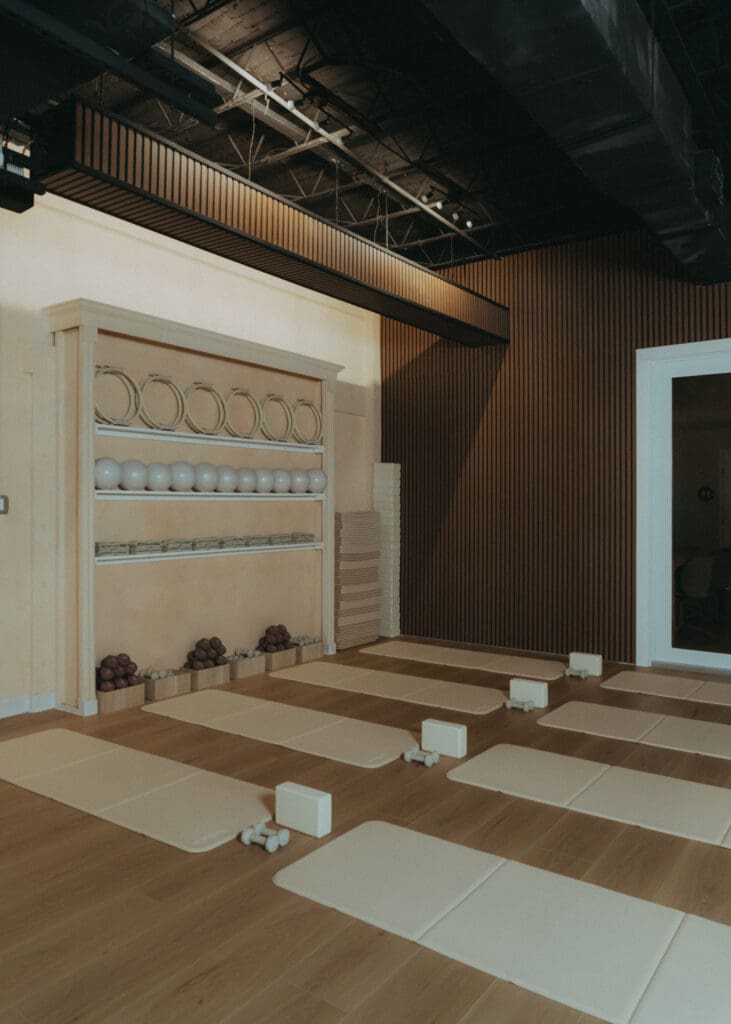 Wide interior photo of modern Pilates studio with reformers, neutral tones, and wood panel walls.