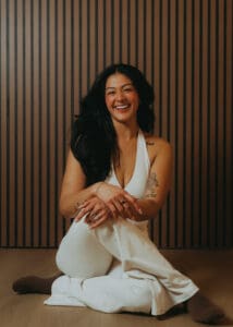 Portrait of Pilates instructor in a white set sitting on the studio floor against a wood slat wall, photographed for personal branding and fitness photography.