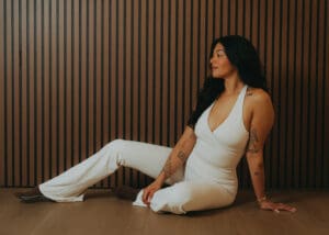 Portrait of Pilates instructor in a white set sitting on the studio floor against a wood slat wall, photographed for personal branding and fitness photography.