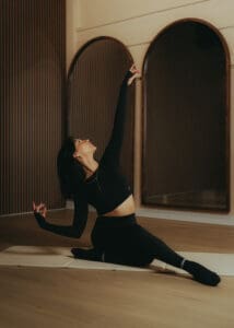 Pilates instructor stretching on mat in warm, moody wellness studio.