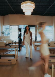 Pilates instructor standing between reformers while team members move in background, photographed for Solace Studio branding photography in Orlando.