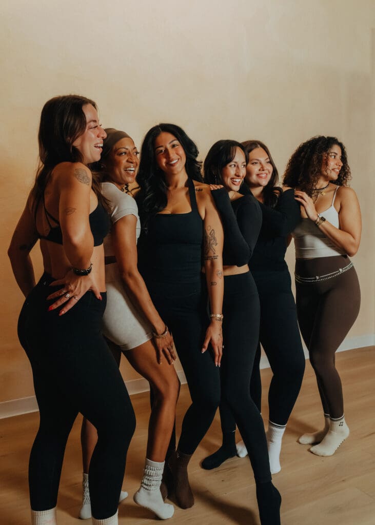 Group of six women in neutral athletic wear smiling together during Pilates branding photoshoot in Orlando studio.