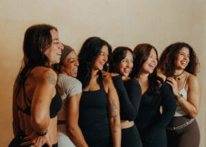 Group of six women in neutral athletic wear smiling together during Pilates branding photoshoot in Orlando studio.