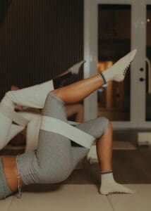 Group of people performing reformer Pilates single leg glute bridge exercise in wellness studio.