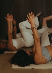 Group of people performing reformer Pilates single leg glute bridge exercise in wellness studio - close-up of hands.