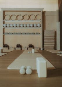 close-up interior photo of modern Pilates studio with mats, blocks, reformers, neutral tones, and wood panel walls.