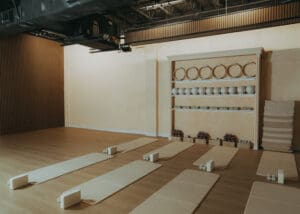 Wide interior photo of modern Pilates studio with reformers, neutral tones, and wood panel walls.