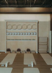 Wide interior photo of modern Pilates studio with reformers, neutral tones, and wood panel walls.