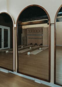 Wide interior photo of modern Pilates studio with reformers, neutral tones, and wood panel walls.