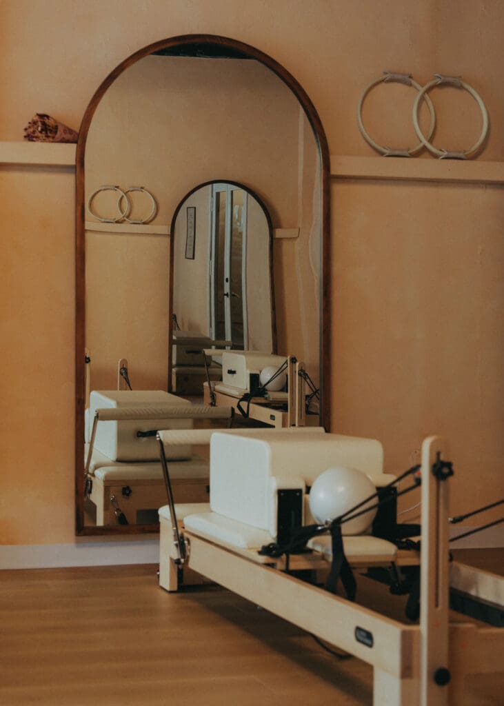 Pilates reformer reflected in arched mirror inside warm, neutral-toned Pilates studio interior in Orlando.