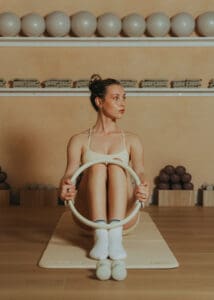 Pilates instructor performing reformer ring exercise on a mat inside a warm, neutral-toned Pilates studio in Orlando.