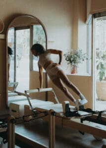 Pilates instructor performing a reformer exercise near large windows at Solace Studio in Orlando, photographed with soft natural light for wellness brand photography.