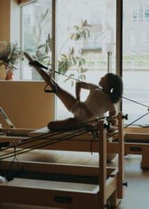 Pilates instructor performing a reformer exercise near large windows at Solace Studio in Orlando, photographed with soft natural light for wellness brand photography.