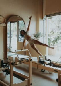 Pilates instructor performing a reformer exercise near large windows at Solace Studio in Orlando, photographed with soft natural light for wellness brand photography.